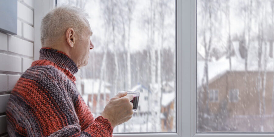 A senior man looking out the window while sipping coffee in winter