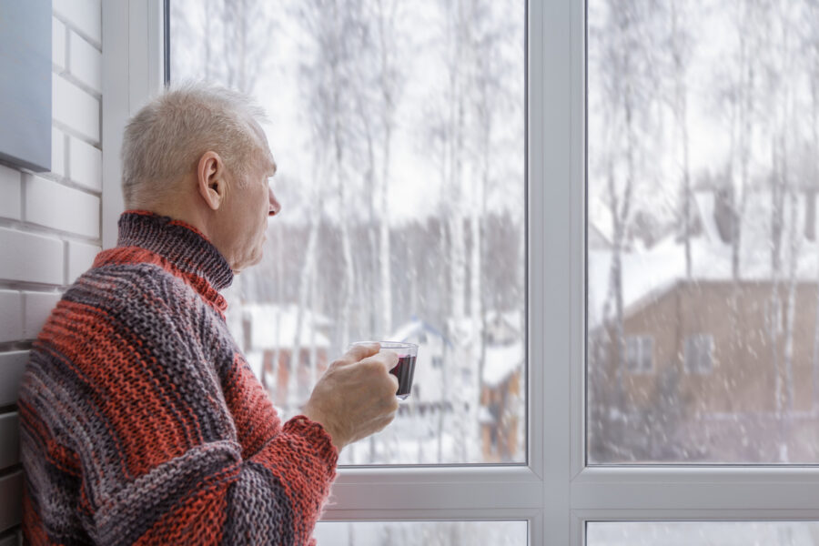 A senior man looking out the window while sipping coffee in winter